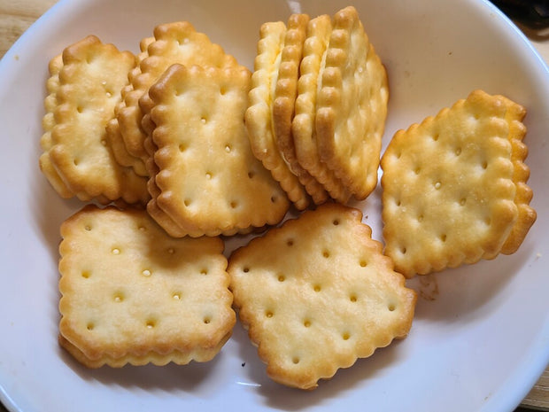 A green and yellow package from the Doki Doki Snack Adventure Crate (10 pcs), perfect for Japanese snack lovers, displays tempting images of mini cream sandwich crackers on the front.
