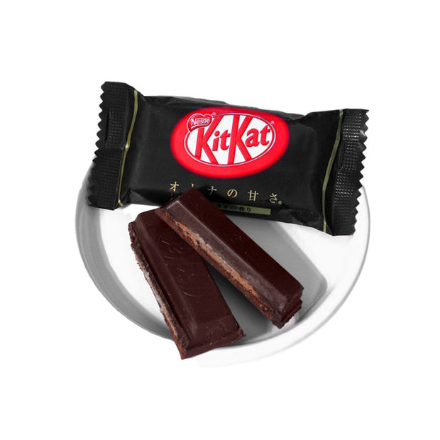 A Japanese Kit Kat: Dark Chocolate (10 pcs) in black packaging sits on a white plate, with two dark chocolate wafer bars beside the wrapper, showcasing this unique Japanese treat crafted for an adult palate.