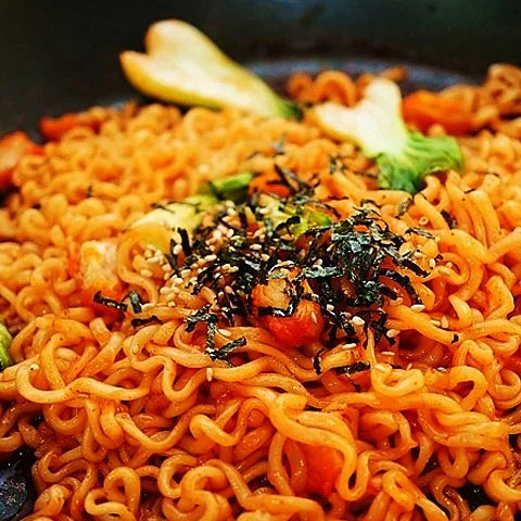 Front view of a Fiery Flavor Crate (Medium) featuring Samyang Buldak instant noodles with a cartoon chicken, noodles, flames, bold Korean and Japanese text, and a visible Halal certification logo—a top pick for spicy snack fans.