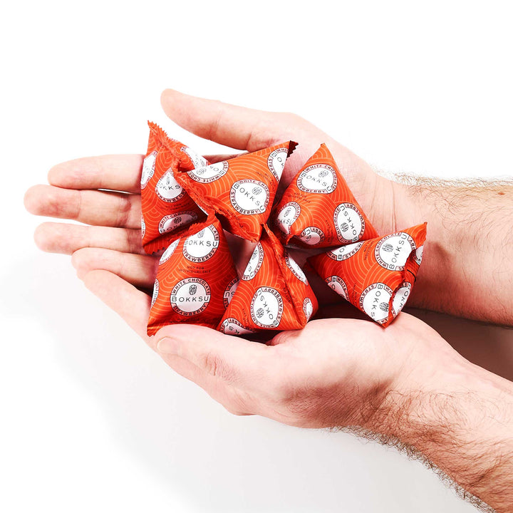 Hands holding several red, triangular snack packages with white and black labels, similar to a Bokksu White Strawberry 6-Piece Box from Bokksu featuring Japanese snacks. thumbnail 5