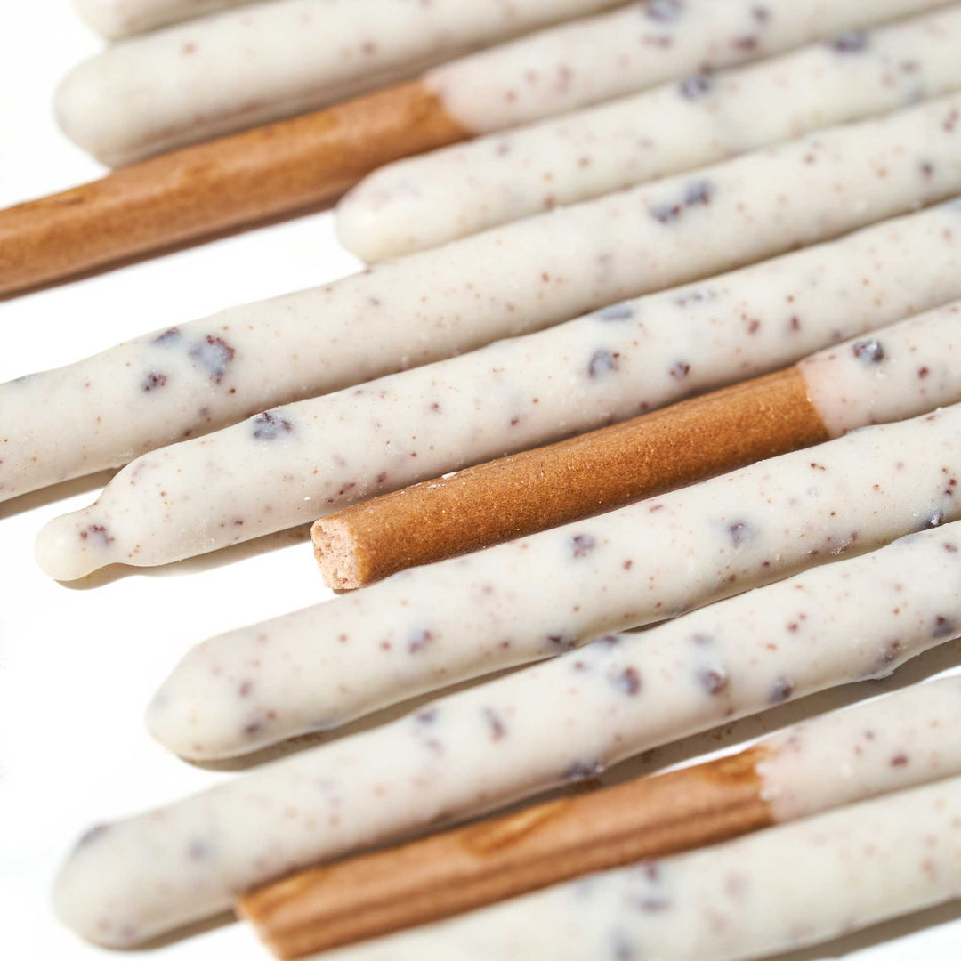 A close-up of Glico's Pocky Family Pack showcases cookie sticks partially coated in white chocolate with cookies & cream specks, neatly arranged in a parallel pattern, ready to be enjoyed.