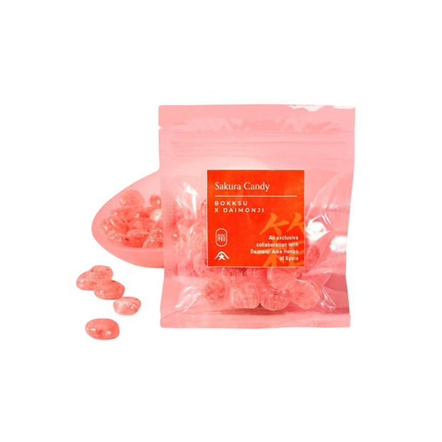 A clear plastic bag from the Japan Crate Medium Crate contains pink hard candies, beautifully displayed on a pink dish and scattered nearby, making it a delightful addition to Japanese snacks.