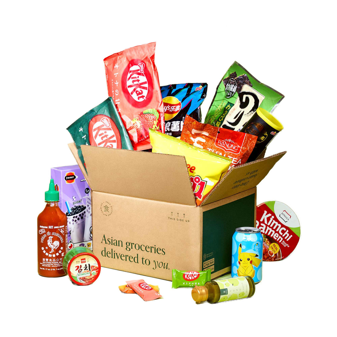 An open box labeled "Asian groceries delivered to you" proudly features a Discovery Pack from Bokksu Market, filled with instant foods and surrounded by a delightful array of Asian snacks, drinks, and sauces.