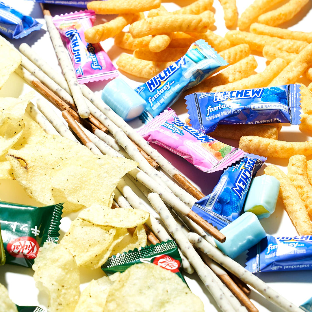 An enticing Bokksu Market Sweet & Savory Snack Mix featuring a variety of snacks such as potato chips, cheese puffs, Pocky sticks, Hi-Chew candies, and KitKat bars is spilled over a white surface. This irresistible assortment effortlessly blends Western favorites with cherished Asian treats.