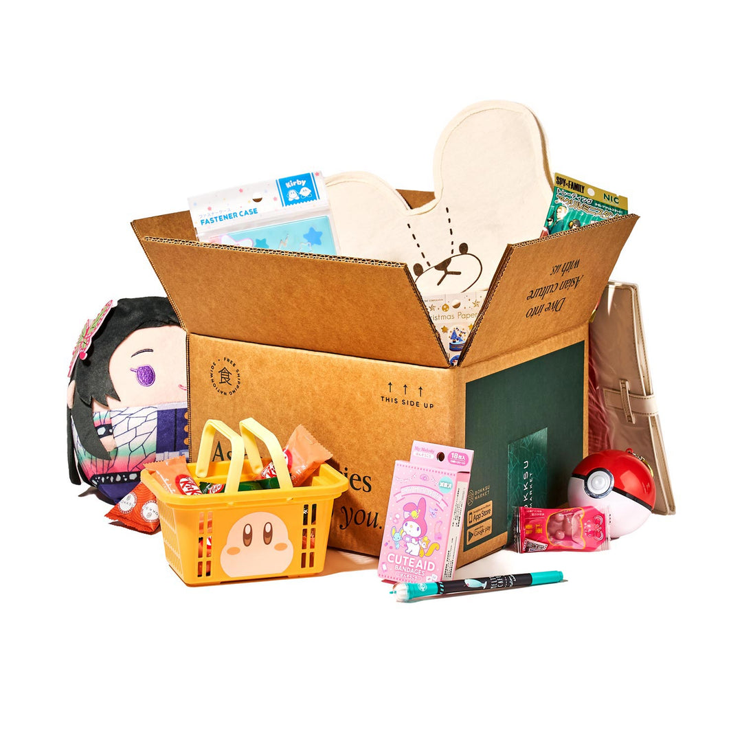 The Bokksu Kawaii Gift Pack - Stationery Surprises & Japanese Chocolate Treats includes Japan's cutest items: a plush toy, decorative fan, Japanese stationery, and snacks. It also features a shopping basket and Poké Ball, all beautifully displayed in an open cardboard box.