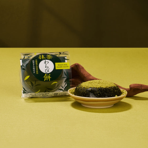 A Matcha Moments Box is shown beside an unwrapped mochi piece on a small plate, topped with vibrant Japanese green tea powder, making a perfect matcha gift.