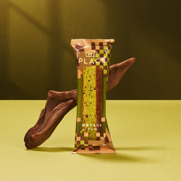 A Matcha Moments Box stands upright against driftwood on a green surface and background, making it a perfect matcha gift box for fans of Japanese green tea treats.