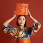 In front of an orange backdrop, a person in a floral kimono lifts the Bokksu Snack Box: Seasons of Japan (FBM) by Bokksu above their head. thumbnail 4
