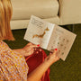 A person sits on a green carpet by a beige sofa, holding an open booklet with a Japan map and snack chart, ready to explore Japanese flavors from their Bokksu Snack Box: Seasons of Japan. thumbnail 25