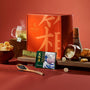 The Bokksu Snack Box: Seasons of Japan includes a variety of Japanese snacks and items like a tea set, crackers, a matcha bar, and candies arranged on a tabletop, with the Bokksu box in the background to celebrate the four seasons. thumbnail 1