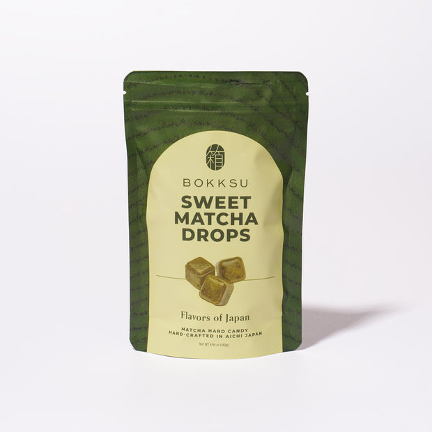 A green and beige bag labeled "Bokksu Sweet Matcha Drops," featuring matcha cubes and the text "Japanese matcha candy handcrafted in Aichi, Japan.