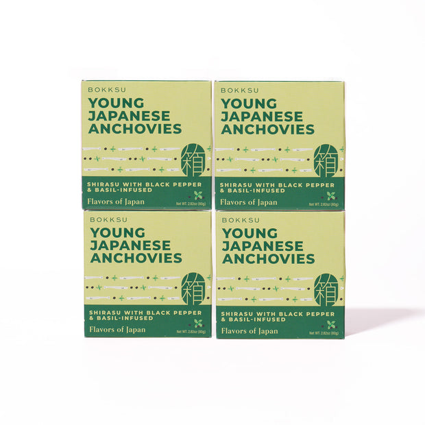 Four boxes of Bokksu Tinned Shirasu Anchovies with Black Pepper and Basil-Infused Oil (4-Pack) are arranged in a square on a white background. Each box contains tender shirasu anchovies infused with basil oil and black pepper, offering a delicate burst of umami flavor.