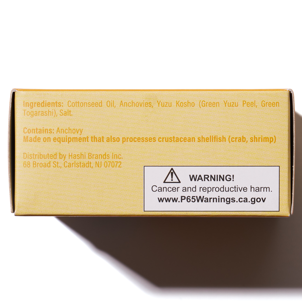 The Bokksu Tinned Shirasu Anchovies with Yuzu Pepper box lists ingredients, allergen info, distributor details, and a cancer and reproductive harm warning. For more info, visit the website provided on the packaging.