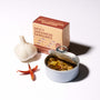 An open tin of Bokksu Spicy Japanese Sardines in olive oil, two dried red chili peppers, a garlic bulb, and the product box are arranged on a white surface. thumbnail 2