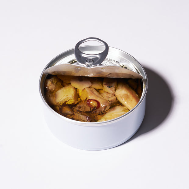 An opened can of Bokksu Spicy Japanese Sardines in olive oil, featuring chunks of fish in liquid, is seen from above against a plain white background.
