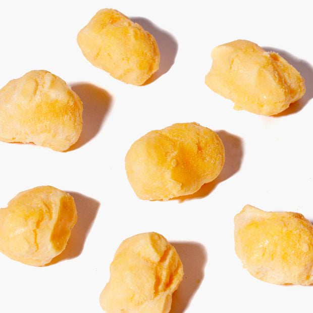 Several yellow cheese curds from the Doki Doki Snack Mix: Japan Mochi Puffs are arranged on a white background, casting small shadows.