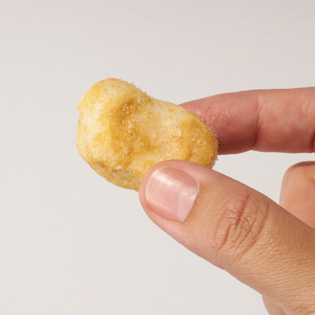 A hand holds a Doki Doki Snack Mix: Japan Mochi Puffs, a small sugar-coated Japanese mochi snack, against a plain white background.