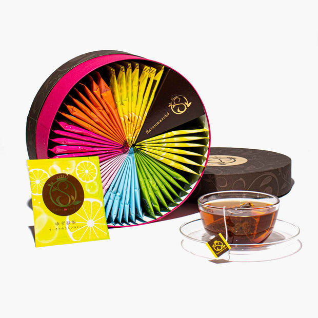 A Kagoshima Seicha Gift Box: Satsumarche Tea Bags (49 pieces, 7 flavors) is shown with a clear glass teacup and a yellow tea packet, all displayed on a white background.