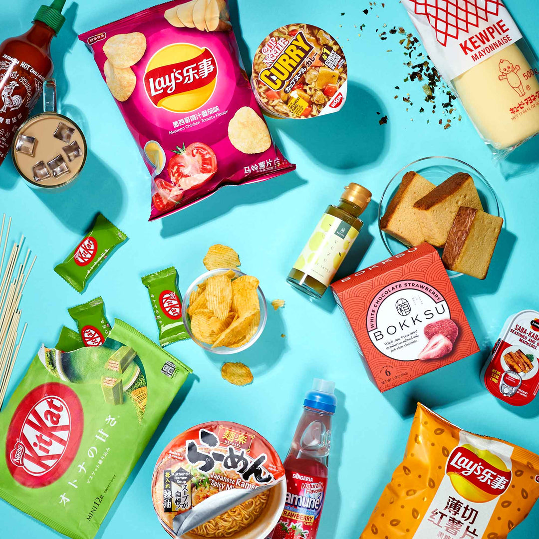 Discover the vibrant Discovery Pack from Bokksu Market, showcasing a colorful array of Asian snacks and drinks like Lay's chips, KitKats, instant noodles, tea, and mayonnaise—all beautifully set against a blue backdrop.