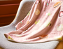 A pink blanket with a fruit pattern is draped over a light gray chair near a window, perfect for relaxing with the Kawaii Gift Pack—Stationery Surprises &amp; Japanese Chocolate Treats. thumbnail 4