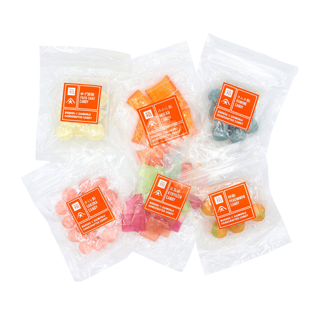 Twelve clear resealable bags of assorted colorful candies in the Daimonji Ame Honpo Handmade Candy Gift Box (6 flavors), each bag with an orange English/Japanese label—ideal for fans of Kyoto sweets and Japanese candy box gifts.