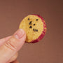 A hand holds a round, golden cookie with a purple edge and black sesame seeds—one of the authentic snacks featured in the April & thumbnail 17