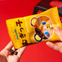 A person pours chocolate-covered treats from a yellow bear-themed package included in the Dagashi Snack Crate (FBA) – Japanese Snack Variety Box with Candy, Chocolate, Cookies, Mochi &amp; Ramune Treats, set against a vibrant red background. thumbnail 9