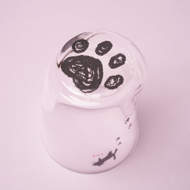 Introducing The Cat Lover’s Box: a charming white cup displayed upside down on a pink surface, adorned with a black paw print design on its bottom and tiny paw prints with a cat silhouette along its side—making it perfect for serving cat-themed snacks or as an adorable addition to any Japanese cat gifts collection.