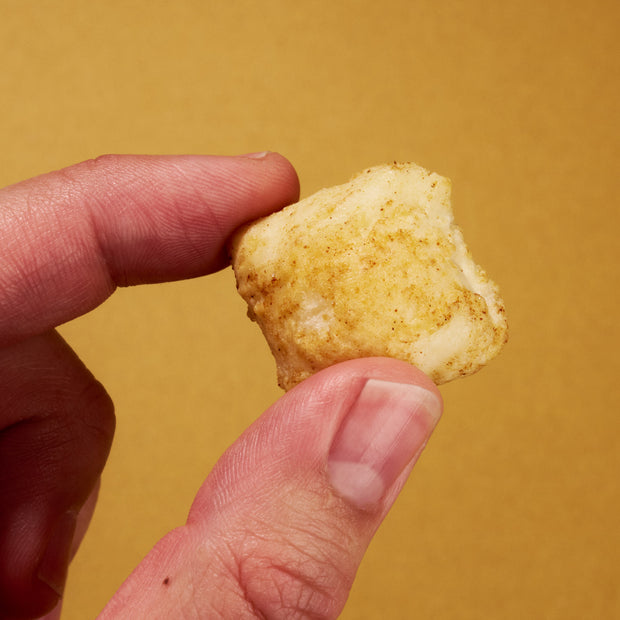 A close-up of a hand holding a seasoned, breaded chicken nugget from April '26 Bokksu: Handpicked in Japan, set against a plain yellow background.