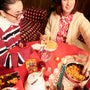 Two people eat noodles with chopsticks at a red table featuring the Spicy Challenge Crate, wrapped gifts, a teapot, and drinks. In the background are a couch and a Christmas tree. thumbnail 2