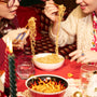 Two people enjoy noodles with chopsticks from the Spicy Challenge Crate, inspired by Japan-exclusive spicy snacks. Glasses of water and candles sit on a red tablecloth, enhancing the bold flavors of this unique crate. thumbnail 4