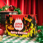 A Spicy Challenge Crate with vibrant flame graphics rests on a checkered surface among festive holiday decorations and tinsel, showcasing an exciting assortment of spicy Japanese snacks. thumbnail 1