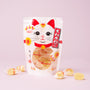 A white snack bag featuring a maneki-neko (beckoning cat) design, filled with individually wrapped yellow candies, makes a charming addition to The Cat Lover’s Box or a delightful Japanese cat gift, displayed against a light pink background. thumbnail 11