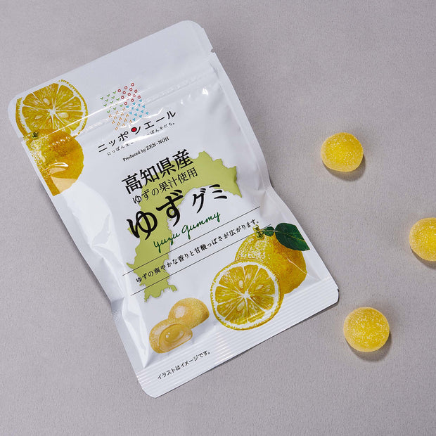 A white package of Japanese Fruits Gummy Box with sliced yuzu fruit images sits beside three yellow gummies on a gray surface—an enticing treat for fans of authentic Japanese flavors.