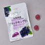 A package from the Japanese Fruits Gummy Box is displayed on a gray surface with two round purple grape gummies beside it. thumbnail 10