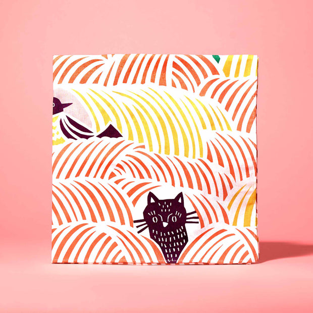 The Cat Lover's Box by Bokksu includes a square cloth with black and yellow Manekineko Jelly-inspired cats on an orange-yellow wave pattern against a playful pink background.