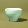 The Japanese Tea Box features a pale green ceramic cup with a smooth, matte finish, ideal for enjoying matcha. It rests on a plain olive-green surface, complemented by a matching background. thumbnail 2