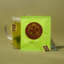 A packet labeled "The Japanese Tea Box" stands in front of a glass mug of matcha tea with a tea bag and tag, set against a plain olive background. thumbnail 4