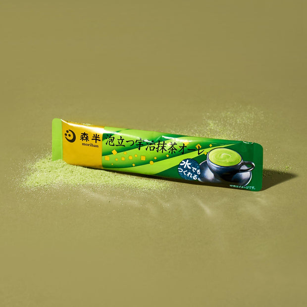 A single-serve stick from The Japanese Tea Box rests on a green surface, with vibrant matcha green tea powder spilled around it.