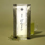 The Japanese Tea Box with Matcha Iri Genmaicha loose green tea leaves scattered beside a glass mug of vibrant green tea, all set on a yellow background. thumbnail 13