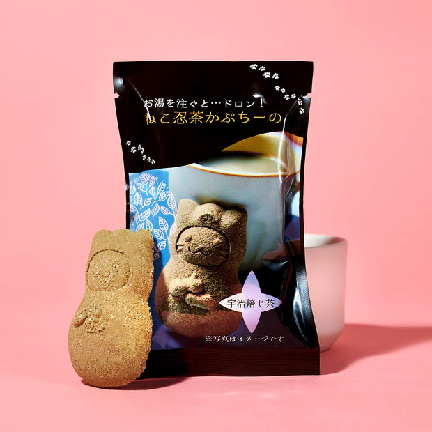 A cat-shaped Manekineko Jelly from The Cat Lover's Box by Bokksu stands before its Japanese-text packaging and a white cup, all against a pink background.