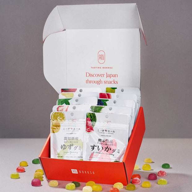 An open Japanese Fruits Gummy Box displays an enticing assortment of colorful Japanese fruit gummies scattered across a gray surface—perfect for discovering authentic Japanese flavors.