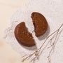 A round chocolate cookie, broken in half on a textured surface beside a tiny twig, reflects the refined simplicity of Japanese snacks featured in the Bokksu Snack Box: Seasons of Japan. thumbnail 12