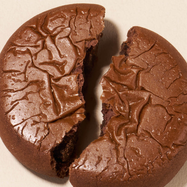 A close-up of a round chocolate cookie broken in half on a light surface, highlighting the rich flavor inspired by Japanese snacks from the Bokksu Snack Box: Seasons of Japan.