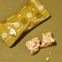 A yellow Kyoto-branded wrapper sits beside two pieces of a nutty treat from the Bokksu Snack Box: Seasons of Japan—ideal for those craving authentic Japanese flavors—on an olive green surface. thumbnail 4
