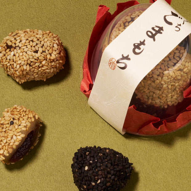 Three sesame-covered confections and a round packaged sweet from the Bokksu Snack Box: Seasons of Japan are arranged on a textured green surface, offering an authentic taste of Japanese snacks.
