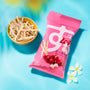 A pink Bokksu Snack Box: Seasons of Japan sits beside a yellow bowl of snack sticks on a blue surface with white flowers nearby—offering a delightful taste of Japan. thumbnail 20