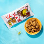 The Bokksu Snack Box: Seasons of Japan sits beside a bowl of square, brown snacks on a blue surface with a yellow flower nearby—offering authentic Japanese flavors for Bokksu fans. thumbnail 22