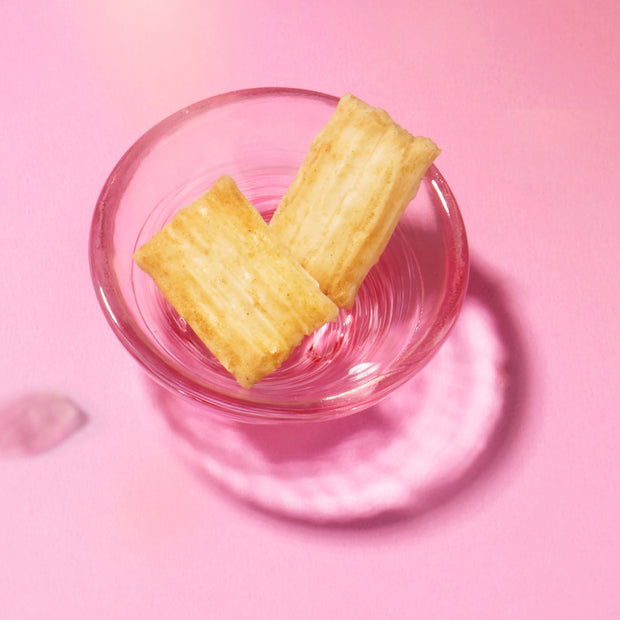 Two rectangular golden puff pastries rest in a pink glass bowl, evoking the authentic flavors of Japan you’ll find in the Bokksu Snack Box: Seasons of Japan, perfect for anyone craving classic Japanese treats.