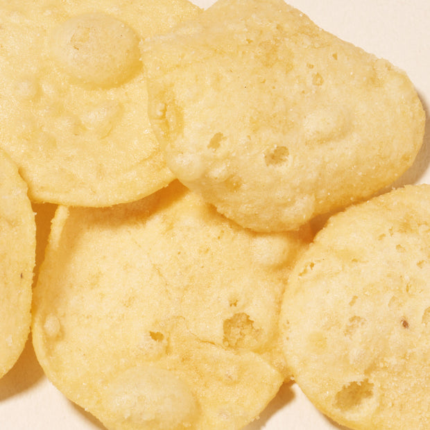 Close-up of crispy, light-yellow Japanese snacks with a bubbled surface, overlapping on a neutral background—experience authentic flavors with the Bokksu Snack Box: Seasons of Japan.